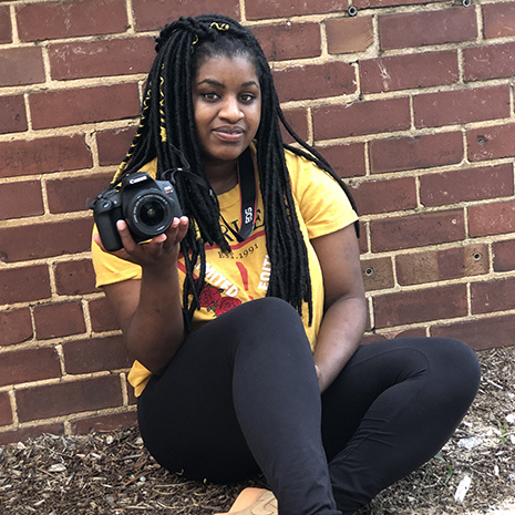 Jaylen Anderson holding a camera while sitting in front of a brick wall