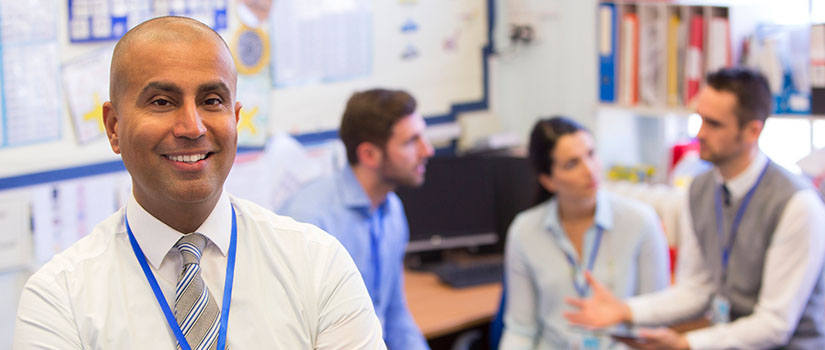 smiling man looks outward as three colleagues discuss in the back of an office