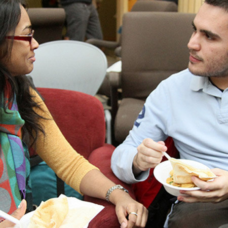 two people speaking and hodling plates of food