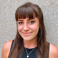 A brown-haired white woman in front of a concrete wall.