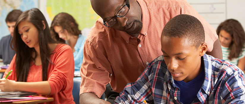 Teacher leaning over student to point at something in a classroom