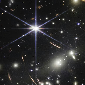 An image from NASA’s James Webb Space Telescope shows the dense galaxy cluster SMACS 0723, filled with thousands of galaxies—from bright ellipticals to faint red spirals—with gravitational lensing stretching distant background galaxies into curved streaks of light.