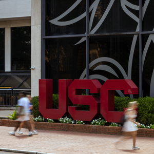 a building with the letters USC in front of windows with people walking in the foreground
